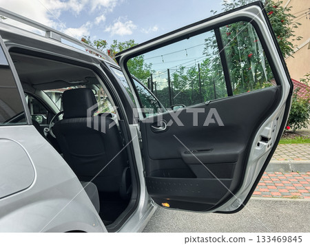 Open door reveals spacious interior of a modern vehicle on a sunny day in an urban neighborhood, inviting an adventure or casual outing with friends and family 133469845