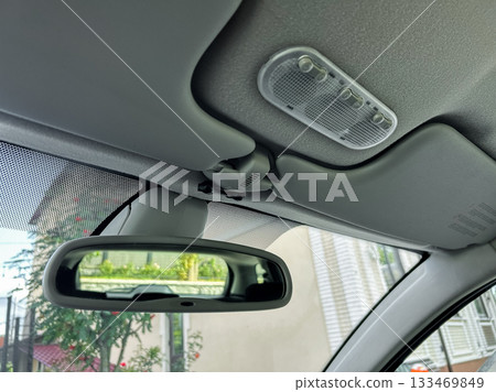 Curious view from inside a car showing overhead lights, a rear-view mirror, and the intriguing outside world peeking through the windshield Curious view from inside a car showing overhead lights, a rear-view mirror, and the intriguing outside world peeking through the windshield 133469849