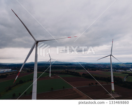 Captivating view of towering wind turbines spinning gracefully above lush fields on an overcast day Captivating view of towering wind turbines spinning gracefully above lush fields on an overcast day 133469860