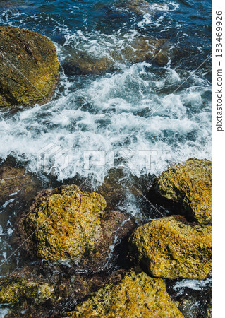 Waves crashing against rugged rocks on a sunny day by the seashore in a tranquil coastal setting 133469926