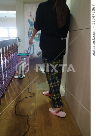 A woman in pajamas uses a vacuum cleaner to clean hardwood floors. 133472067