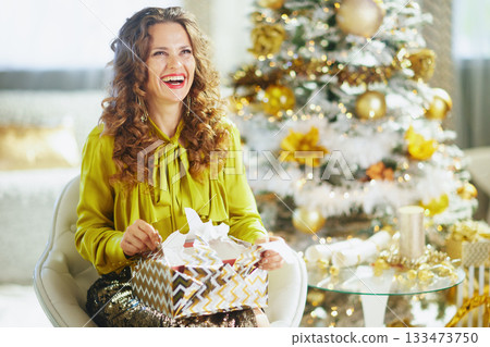 Elegant Woman Joyfully Opening a Christmas Gift Elegant Woman Joyfully Opening a Christmas Gift 133473750