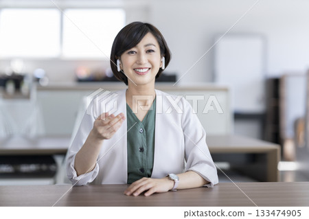 A businesswoman in her 30s wearing earphones and talking while looking at the camera 133474905