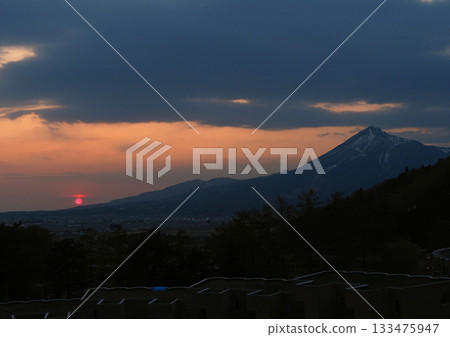 The sun setting at the foot of Mount Bandai. The silhouette of the mountain and the bright red sun are striking and beautiful. The sun setting at the foot of Mount Bandai. The silhouette of the mountain and the bright red sun are striking and beautiful. 133475947
