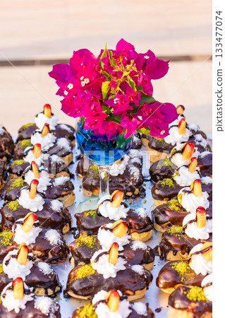 Chocolate Eclairs with Cream and Flowers in Glass Vase Dessert Table Decoration. 133477074