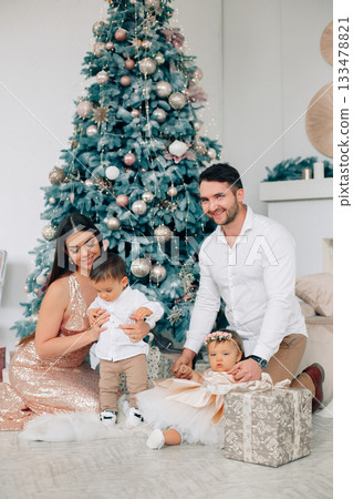 Family celebration in a cozy room with a Christmas tree and children opening gifts in a festive atmosphere Family celebration in a cozy room with a Christmas tree and children opening gifts in a festive atmosphere 133478821