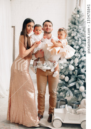 Family celebrates a joyful moment together in elegant attire next to a beautiful Christmas tree decorated with white ornaments and lights Family celebrates a joyful moment together in elegant attire next to a beautiful Christmas tree decorated with white ornaments and lights 133478841