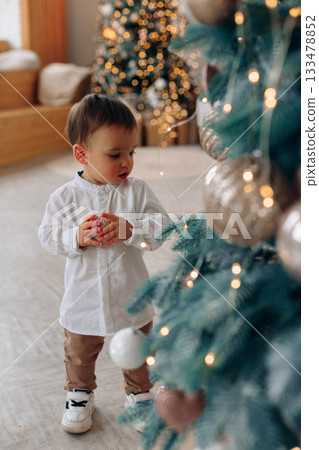 Child explores Christmas tree decorations in a cozy living room during the holiday season 133478852