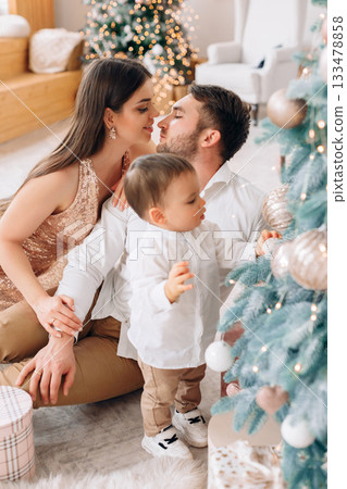 Family enjoys a cozy holiday moment by the Christmas tree while decorating and celebrating together Family enjoys a cozy holiday moment by the Christmas tree while decorating and celebrating together 133478858