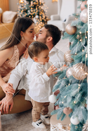 Family enjoying a festive moment by the Christmas tree with decorations and warm lights in a cozy living room setting during the holiday season Family enjoying a festive moment by the Christmas tree with decorations and warm lights in a cozy living room setting during the holiday season 133478859