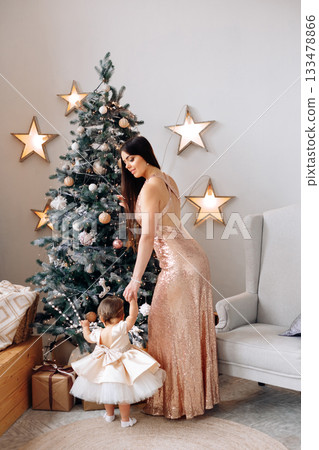 Holiday celebration with a mother and daughter near a decorated Christmas tree in a cozy living room filled with festive decorations 133478866