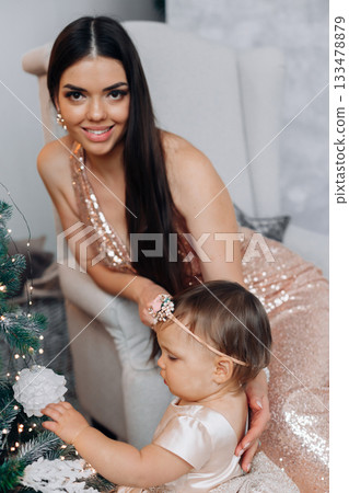 Mother and daughter enjoying a festive moment together by the Christmas tree during a holiday celebration at home in the evening 133478879