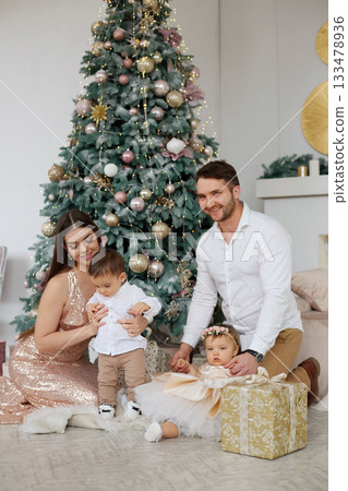 Family celebration with children near Christmas tree in cozy living room during festive season Family celebration with children near Christmas tree in cozy living room during festive season 133478936