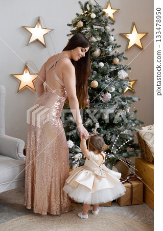 Mother and daughter celebrating holiday season in festive attire near Christmas tree Mother and daughter celebrating holiday season in festive attire near Christmas tree 133478950