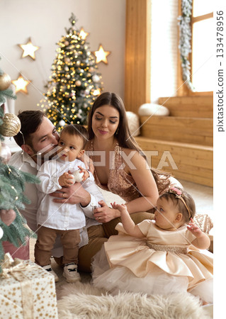 Family gathering in a cozy living room with children celebrating the holidays and enjoying time together by the Christmas tree Family gathering in a cozy living room with children celebrating the holidays and enjoying time together by the Christmas tree 133478956