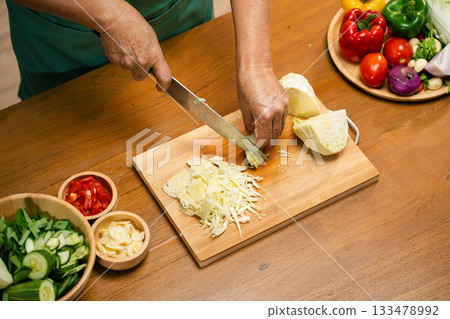 Closeup of male hands slicing Cabbage on a wooden board in the kitchen, preparing to cook. Closeup of male hands slicing Cabbage on a wooden board in the kitchen, preparing to cook. 133478992