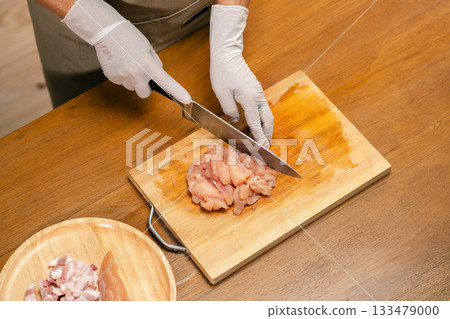 Asian man's hands cutting chicken on a wooden cutting board in the kitchen, preparing to cook. Asian man's hands cutting chicken on a wooden cutting board in the kitchen, preparing to cook. 133479000