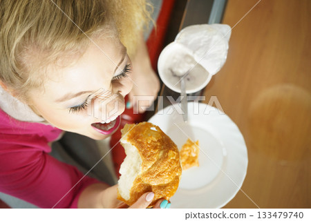 Woman eating croissant and yoghurt Woman eating croissant and yoghurt 133479740