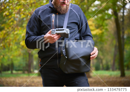 Enthusiast holds a drone controller, ready to capture breathtaking scenes in a vibrant park with golden autumn leaves surrounding. 133479775