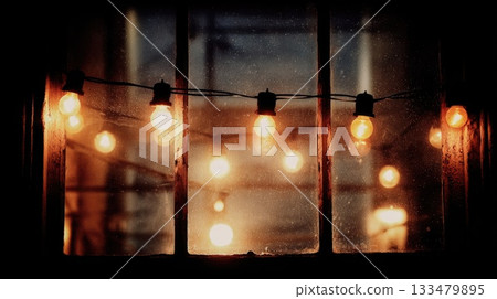 Warm glow of string lights illuminating a cozy evening through a window at twilight 133479895