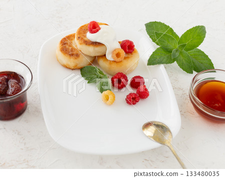 Curd fritters with sour cream, raspberries, strawberry jam and honey. Curd fritters with sour cream, raspberries, strawberry jam and honey. 133480035