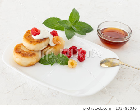 Curd fritters with sour cream, raspberries and honey. 133480036