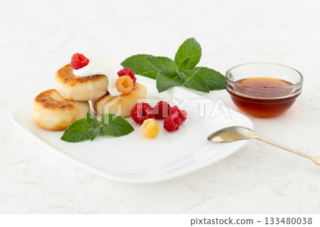 Curd fritters with sour cream, raspberries and honey. 133480038