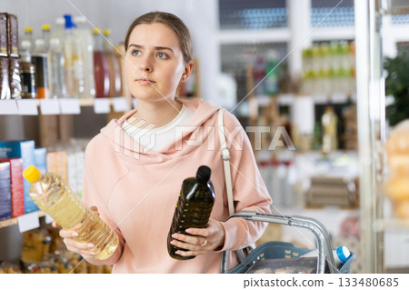 Girl customer in supermarket examines oil, chooses food-stuff in grocery Girl customer in supermarket examines oil, chooses food-stuff in grocery 133480685