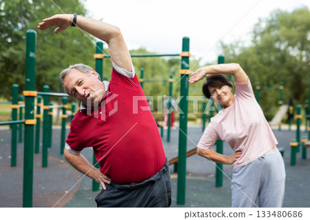 Happy and healthy. Mature family couple in sportswear doing gymnastics together at outdoor gym. Man and woman 133480686