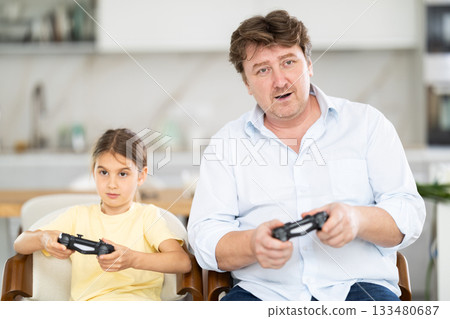 Family, gaming and entertainment concept - happy father and little daughter with gamepads playing video game Family, gaming and entertainment concept - happy father and little daughter with gamepads playing video game 133480687