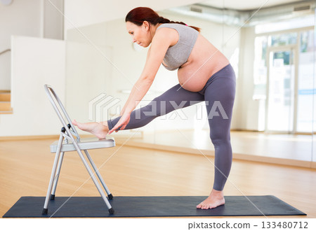 Pregnant woman is engaged in yoga. Chair exercises 133480712