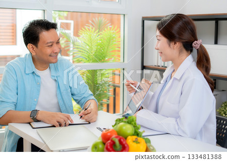 Asian nutritionist using tablet to explaining personalized meal plan with AI to patient. Asian nutritionist using tablet to explaining personalized meal plan with AI to patient. 133481388