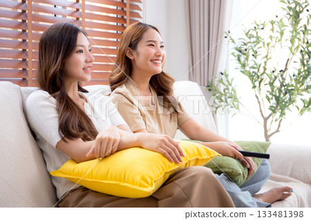 Two young asian woman watching TV together in a cozy living room at home with happy. 133481398