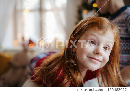 Portrait of small girl indoors at home at Christmas, wearing pyjamas. 133482012