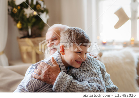 Boy spending Christmas time with senior grandfather indoors at home. 133482020