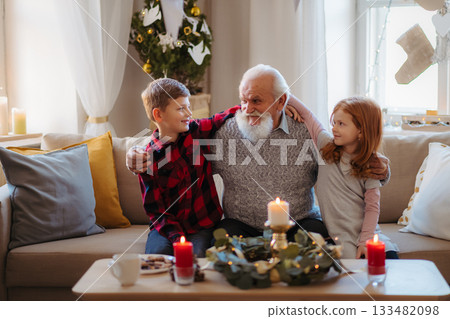 Kids spending Christmas time with senior grandfather indoors at home. 133482098