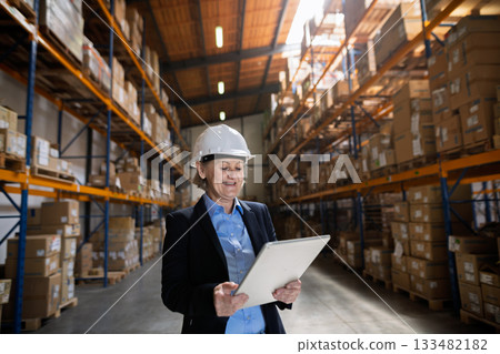 Elderly warehouse manager or supervisor reading document in clipboard. 133482182