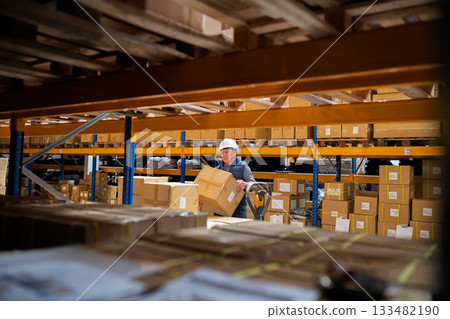 Senior male warehouse worker unloading boxes from a pallet truck. 133482190