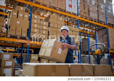 Senior male warehouse worker unloading boxes from a pallet truck. 133482211