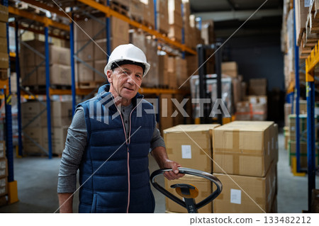 Older male warehouse worker pulling a pallet truck. 133482212