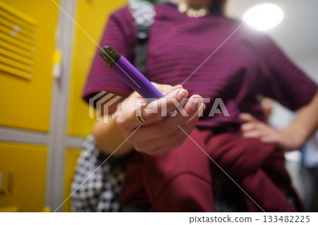 Teen girl holding a vape device in school hallway. Teen girl holding a vape device in school hallway. 133482225