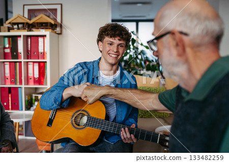 Group of elderly people singing together with young volunteer playing guitar. Group of elderly people singing together with young volunteer playing guitar. 133482259
