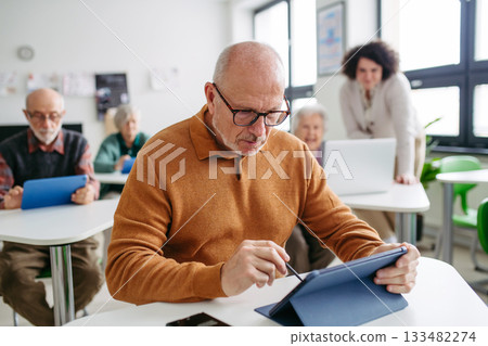 Senior man learning digital skills with tutor support in community center. 133482274