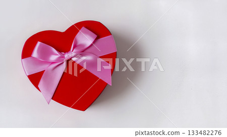 Red heart-shaped gift box tied with a pink satin bow on a white background. 133482276