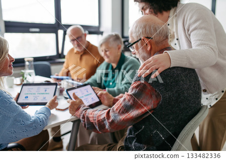 Group of senior people learning digital skills with tutor help. 133482336
