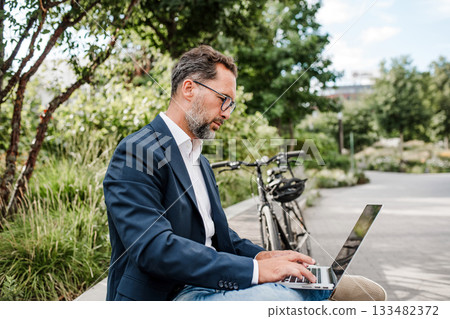Manager working in urban park, making phone call and typing on laptop. Manager working in urban park, making phone call and typing on laptop. 133482372