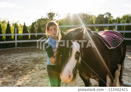 Girl grooming a horse at sunset. 133482421