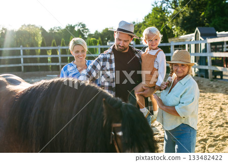 Farmer family standing in horse paddock with pony. 133482422
