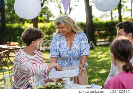Senior woman serving food during family grill party. 133482485