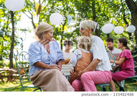 Smiling senior woman with grandchild and daughter at family gathering. 133482486